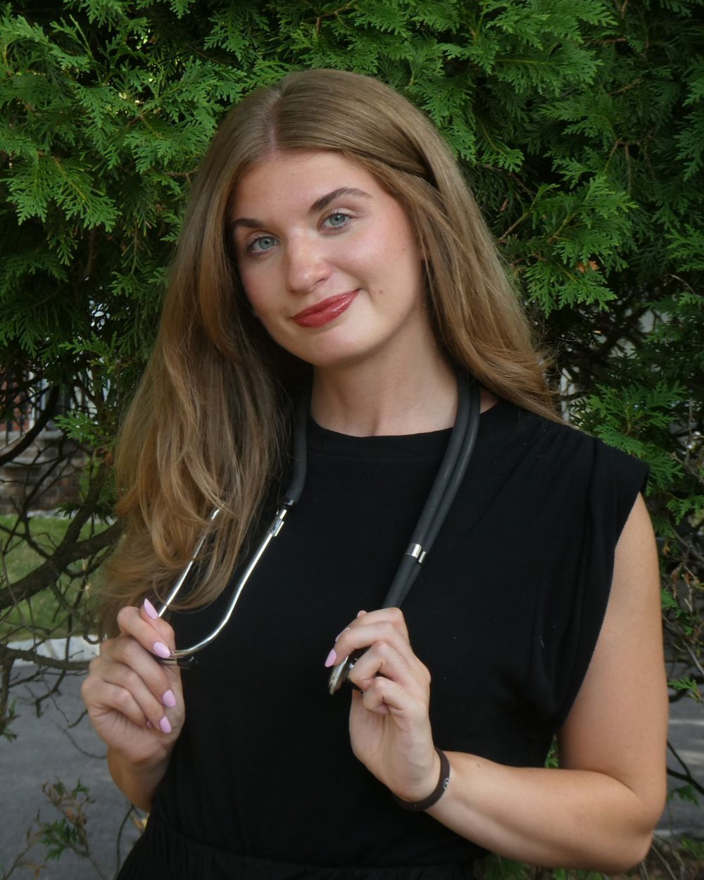 Elyse Fearon outdoors among evergreens, holding her stethoscope