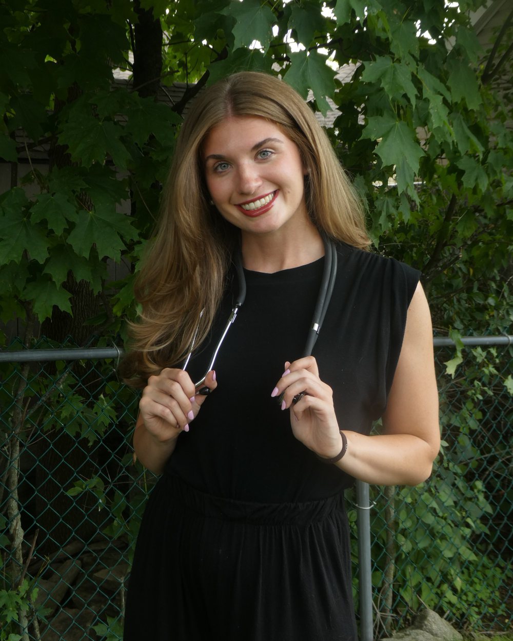 Elyse Fearon smiling outdoors, holding her stethoscope