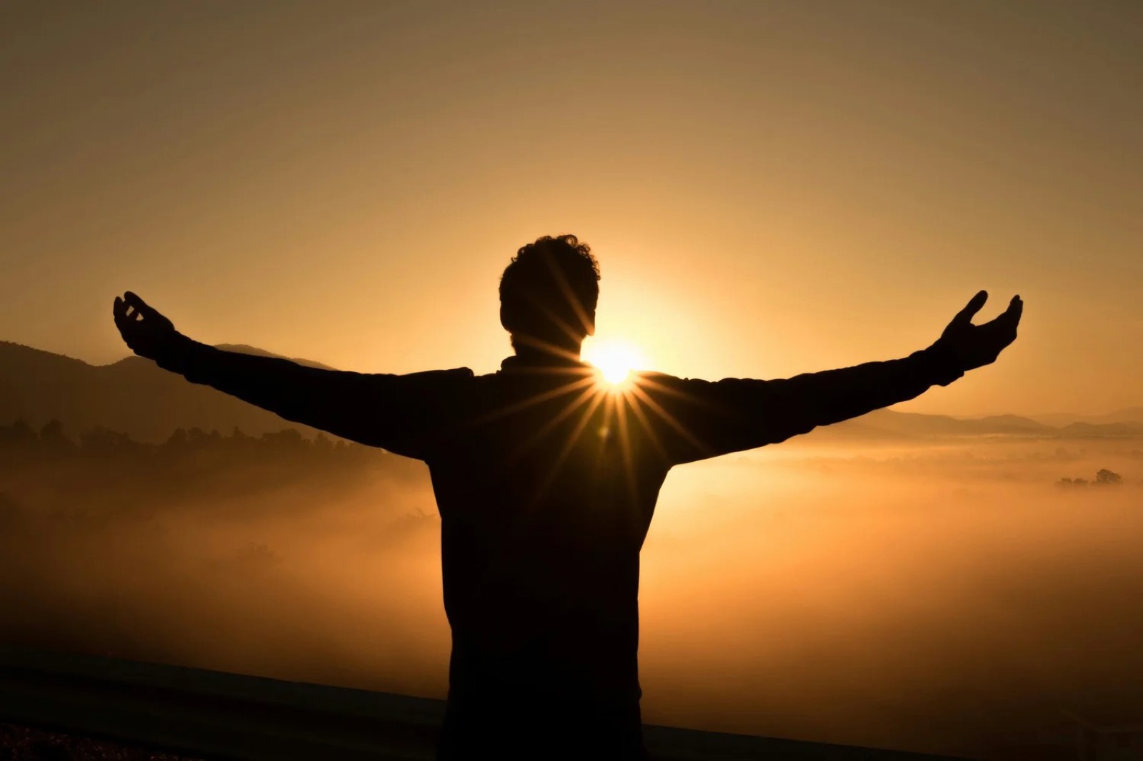 A person with arms raised toward a golden sunrise